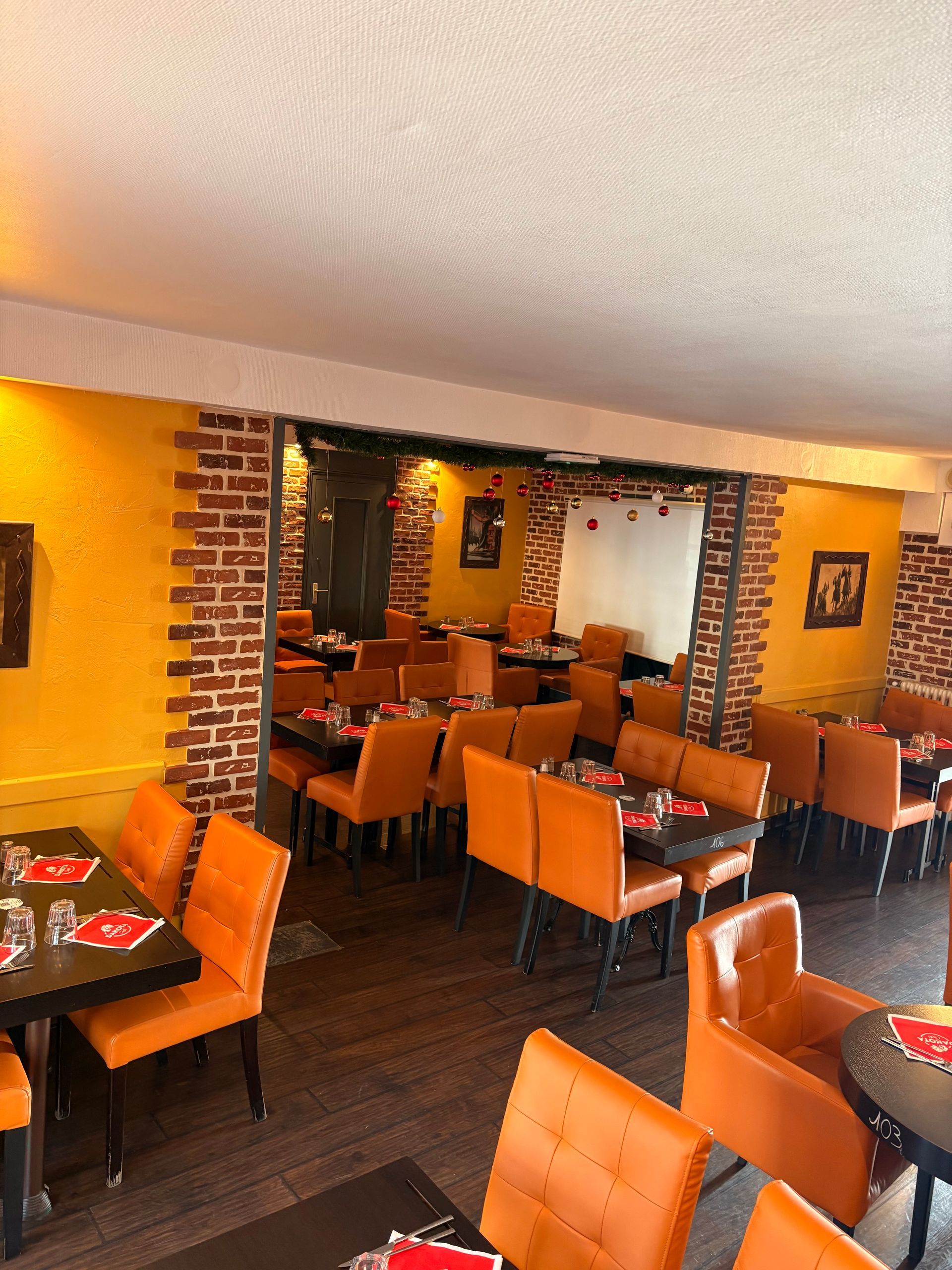 Intérieur de restaurant avec chaises orange, tables sombres, murs jaunes et éléments en brique.