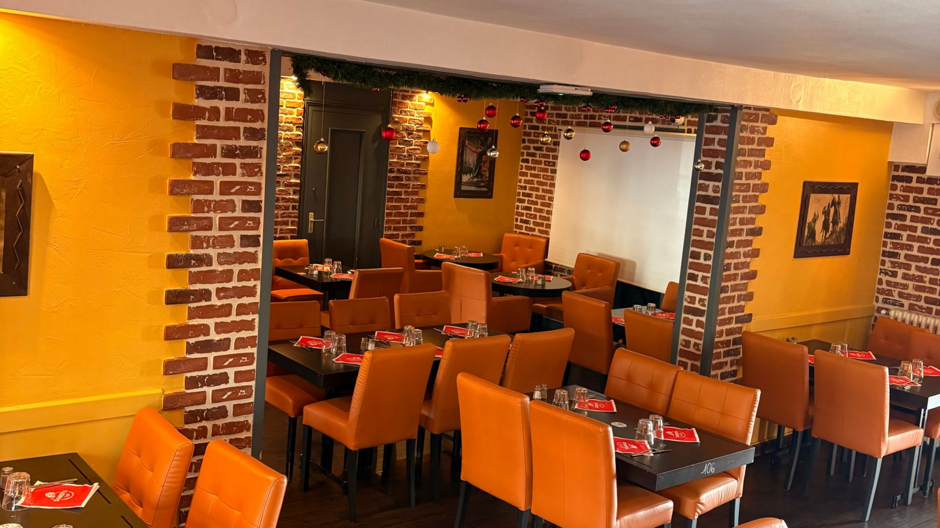 Intérieur de restaurant avec chaises orange, tables sombres, murs jaunes et éléments en brique.