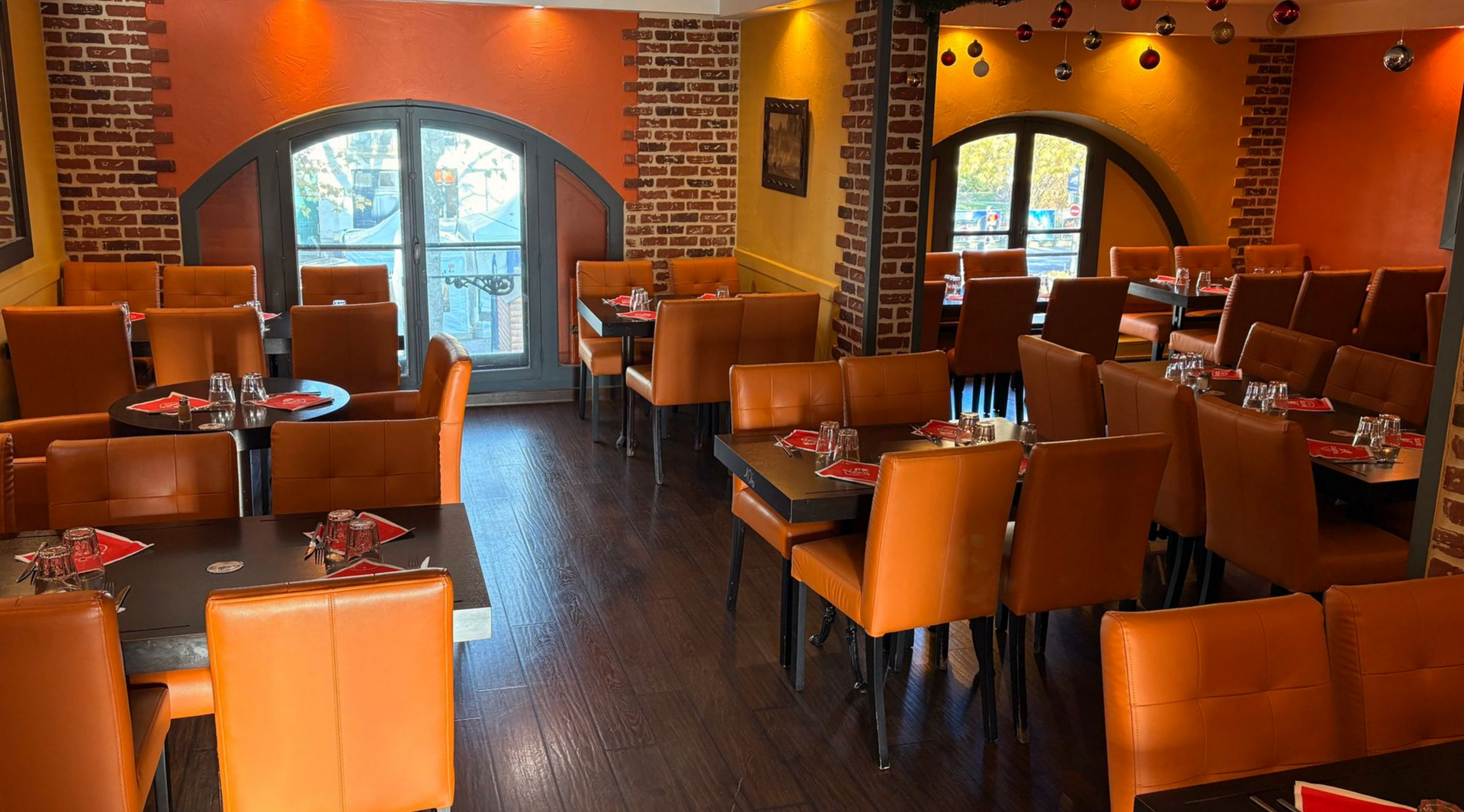 Intérieur de restaurant avec chaises et tables orange, et éléments en briques apparentes ; arches et fenêtres visibles.