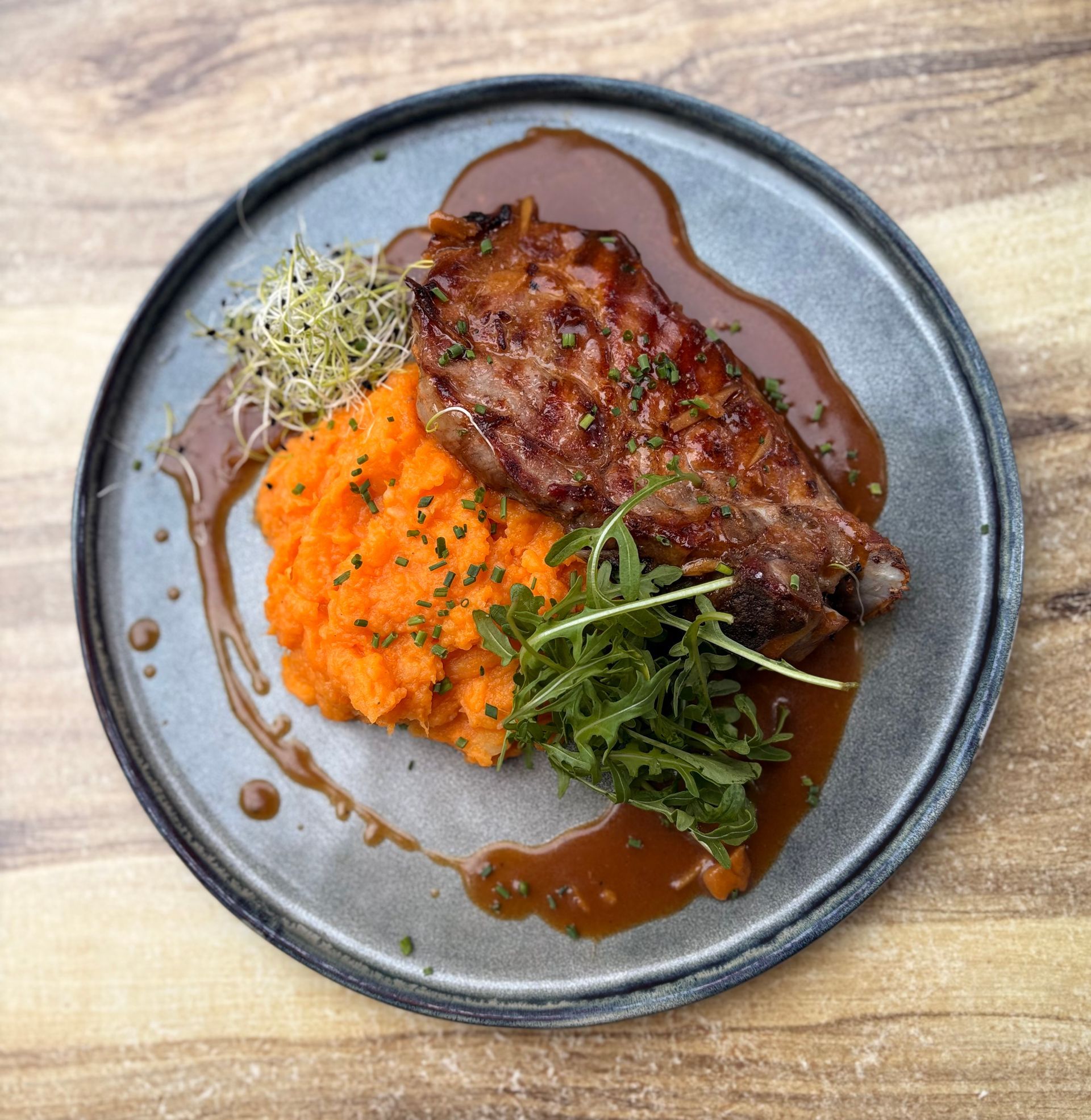 Steak accompagné de purée de patates douces à l'orange, de légumes verts et de sauce, servi sur une assiette grise.