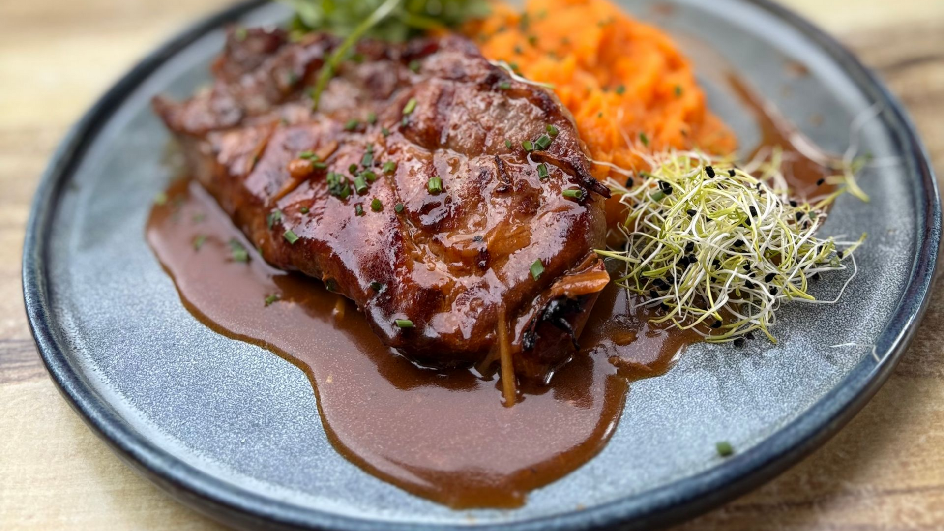 Steak nappé de sauce brune, servi avec une purée de carottes et des germes.