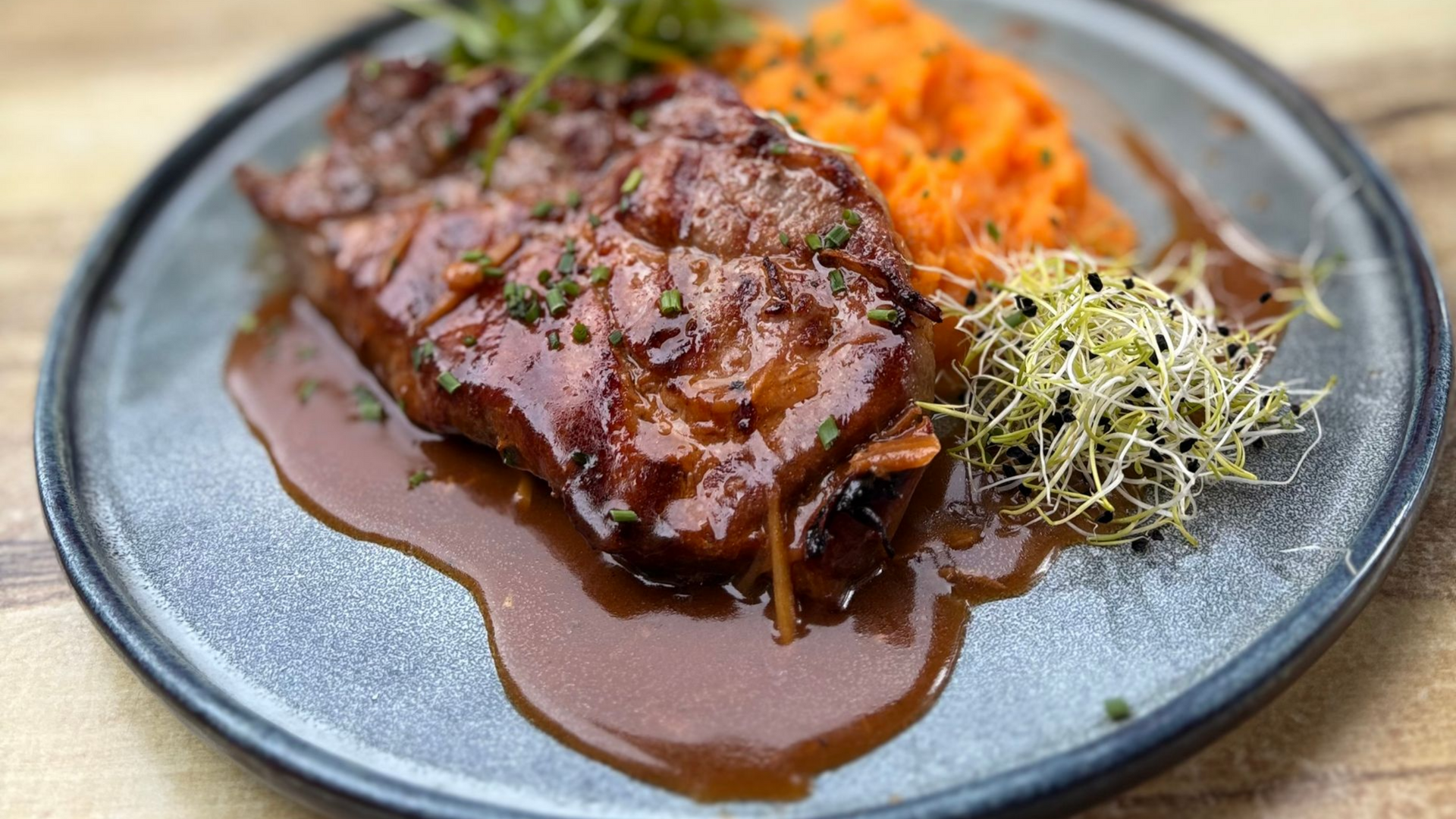 Viande braisée en sauce, servie avec de la purée de patates douces et des germes sur une assiette grise.