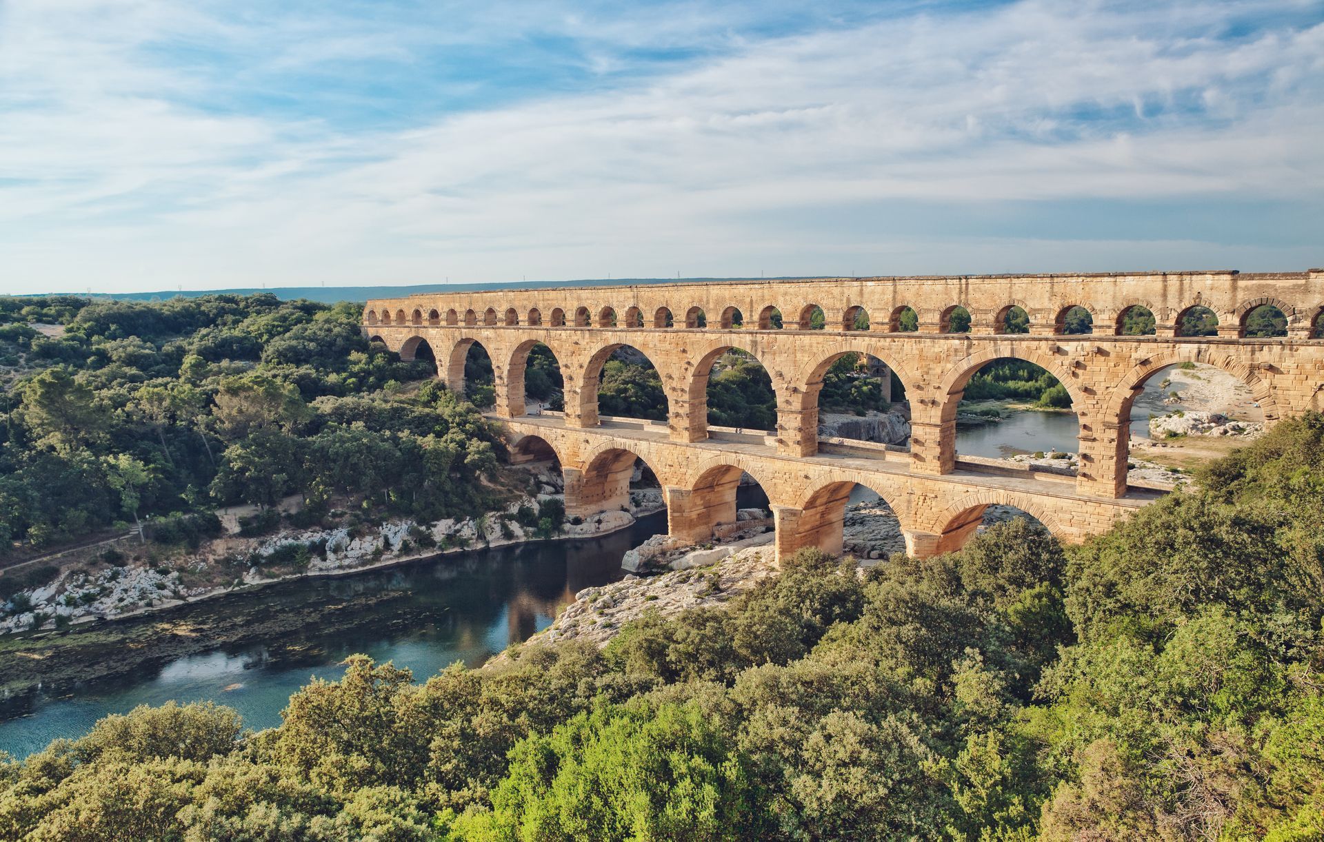 Le Pont du Gard, enjambe une rivière, entouré d'une végétation.