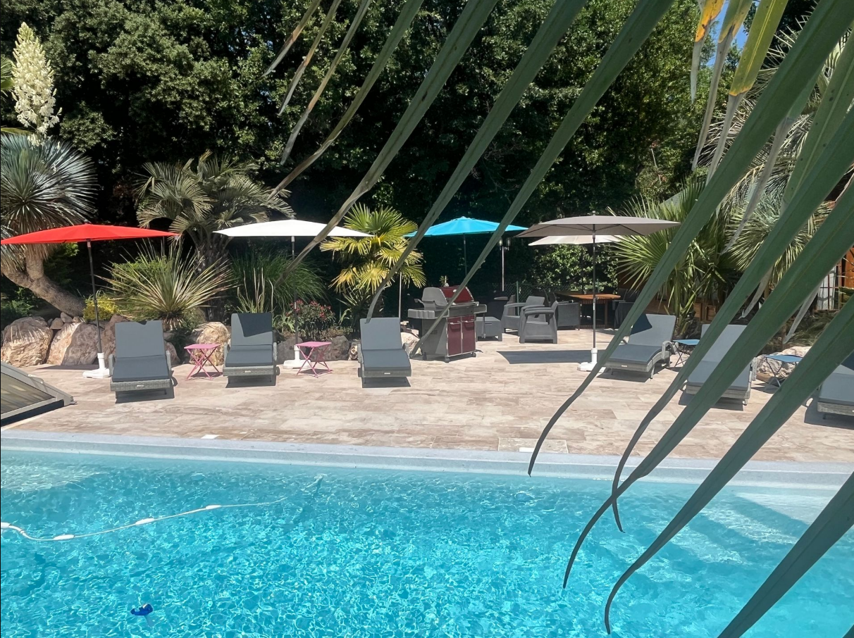 Piscine ; chaises longues, parasols et personnes en arrière-plan sur une terrasse.