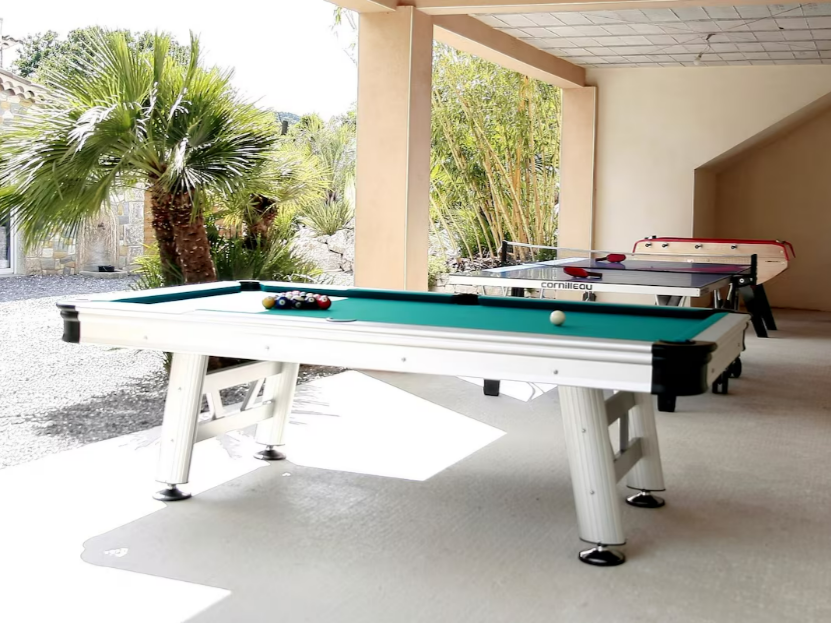 Table de billard blanche, table de ping-pong et bayby-foot, sous un patio couvert près d'un palmier.