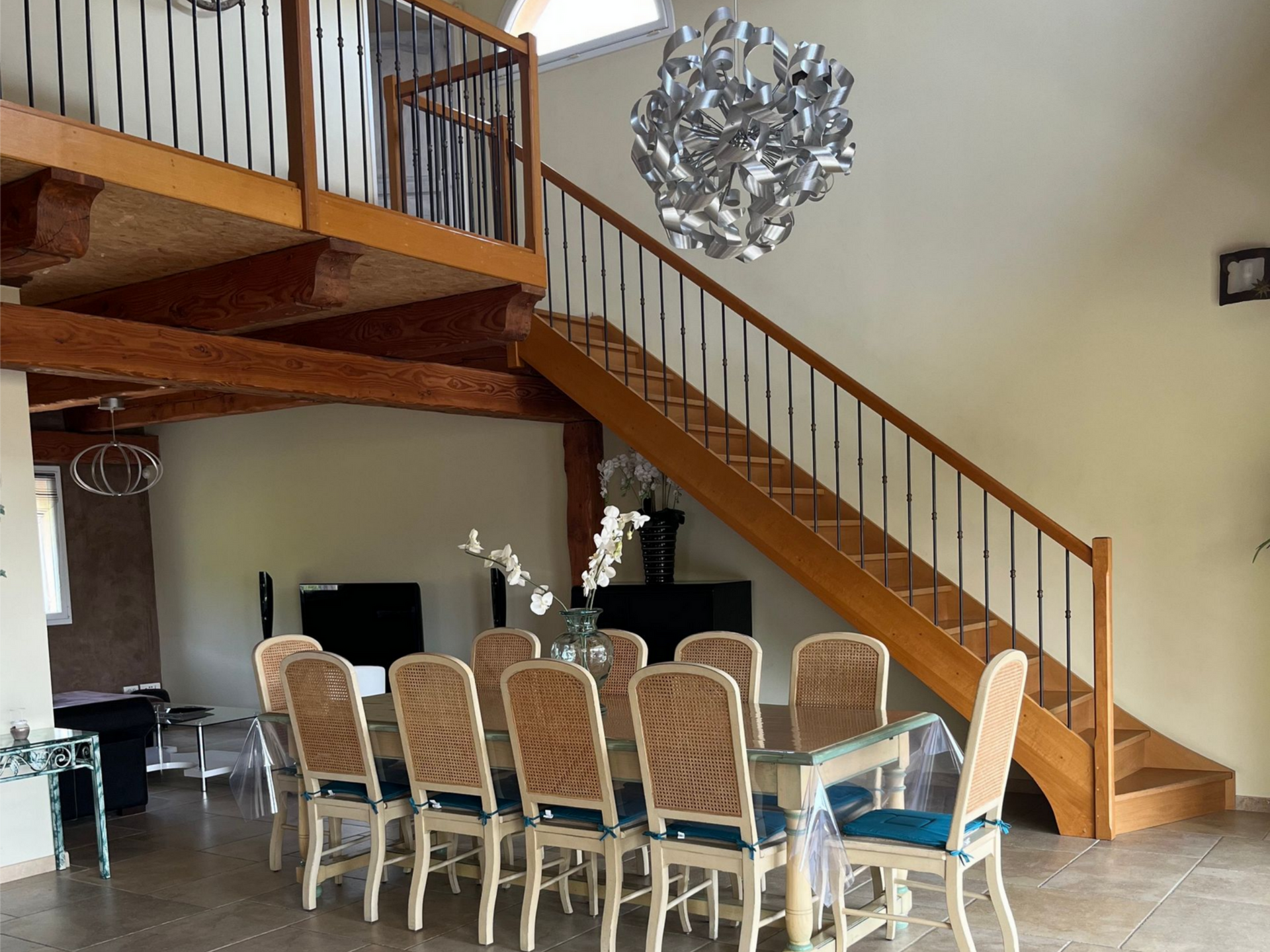 Salle à manger avec grande table, chaises et escalier menant à une mezzanine.