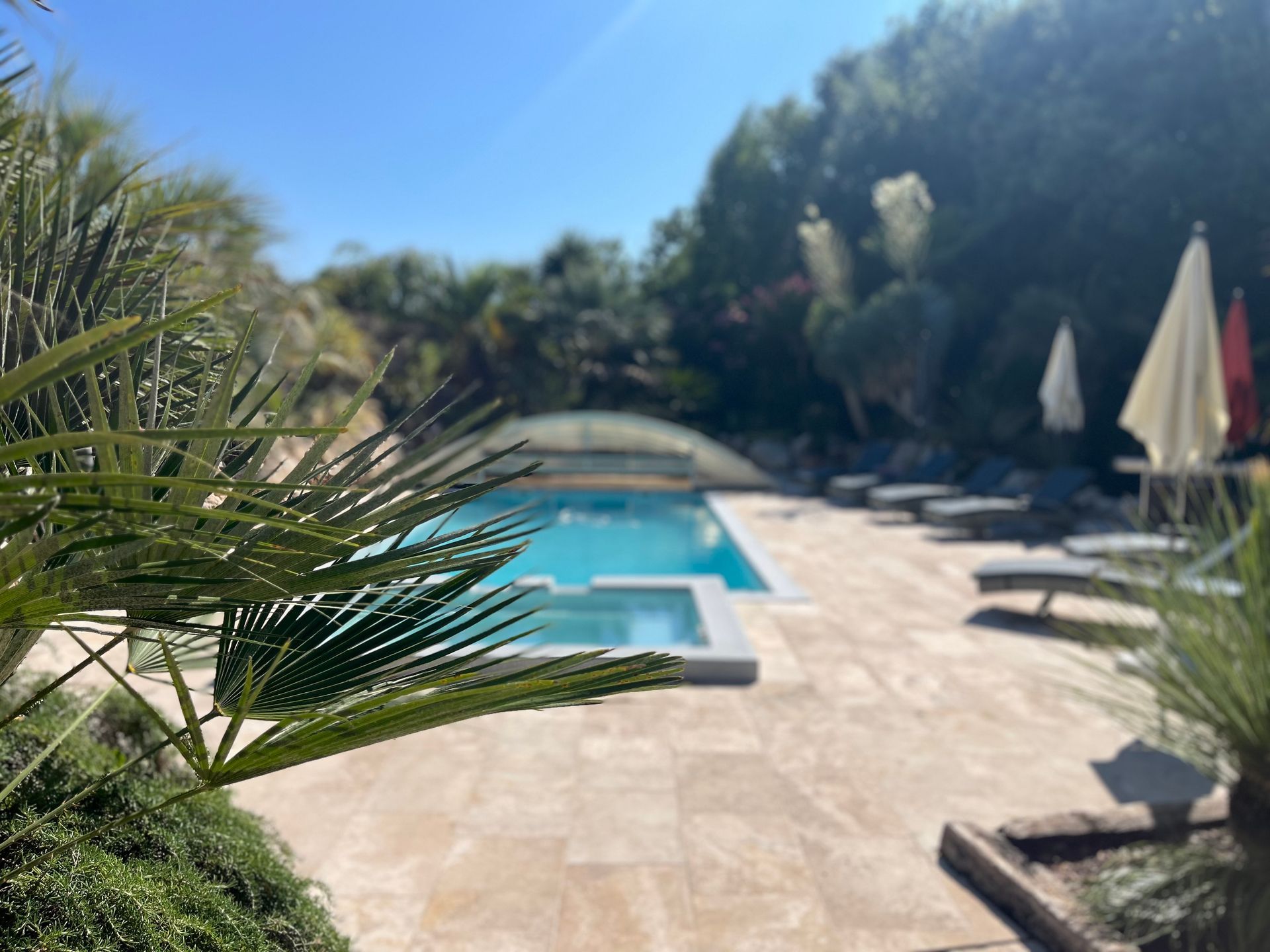 Piscine ; chaises longues, parasols et personnes en arrière-plan sur une terrasse.