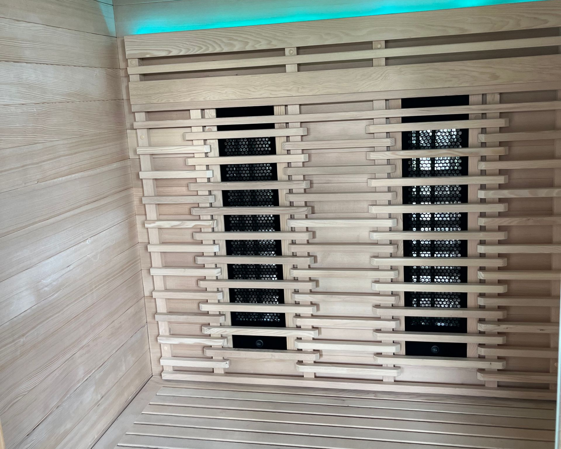 Intérieur d'un sauna lambrissé avec banquettes, radiateurs infrarouges et panneau de commande