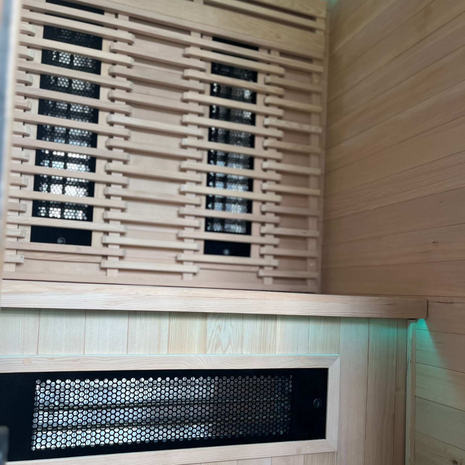 Intérieur d'un sauna lambrissé avec banquettes, radiateurs infrarouges et panneau de commande