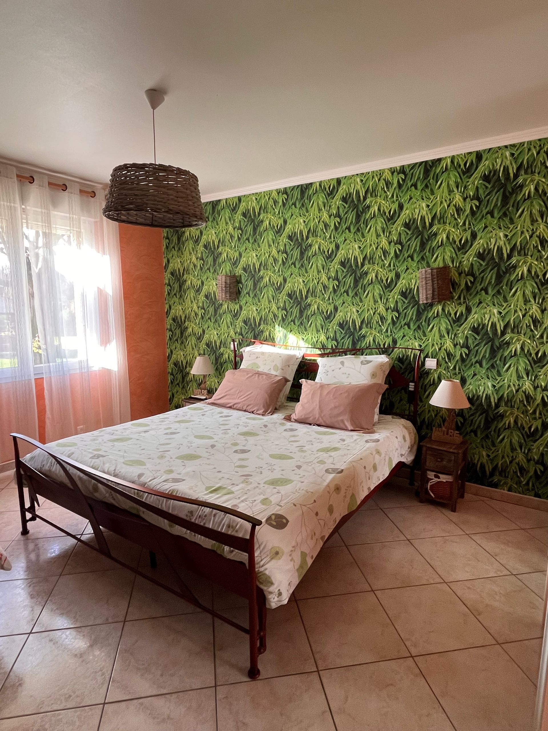 Chambre avec fresque tropicale, lit en métal, commode en bois.