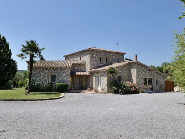 Maison en pierre du Domaine L'Oasis de Boisset avec allée de gravier, palmier et pelouse verte.