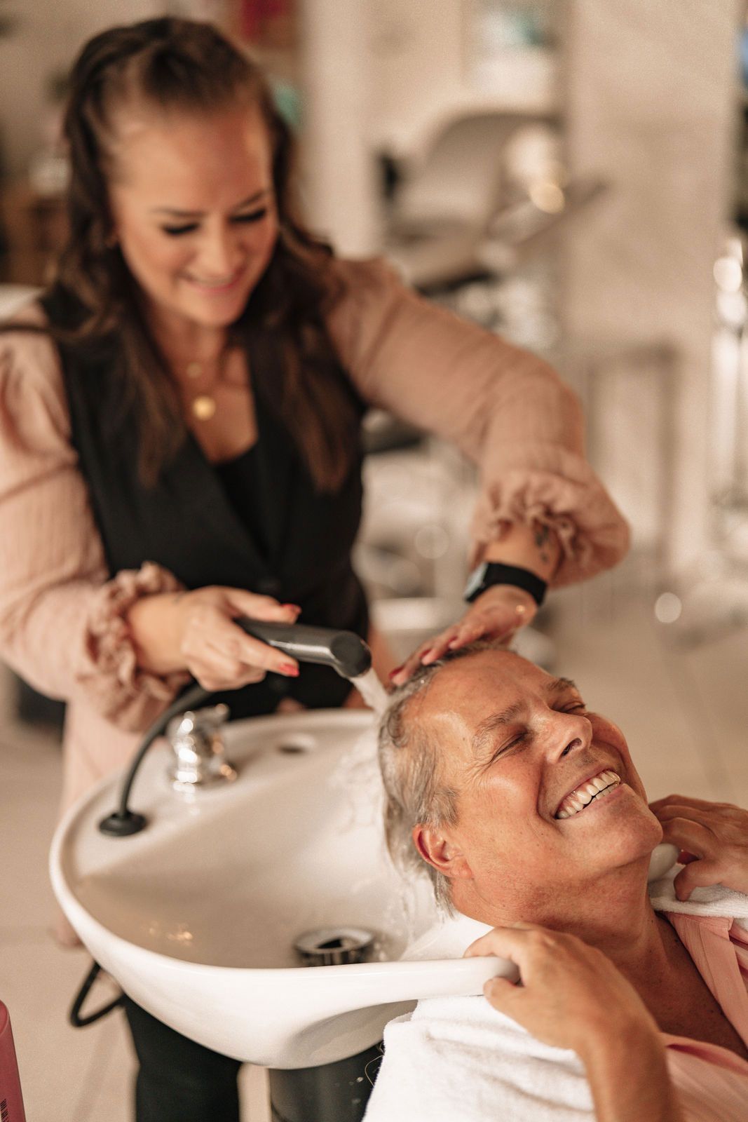 Eine Frau lässt sich in einem Salon von einem Friseur die Haare waschen.