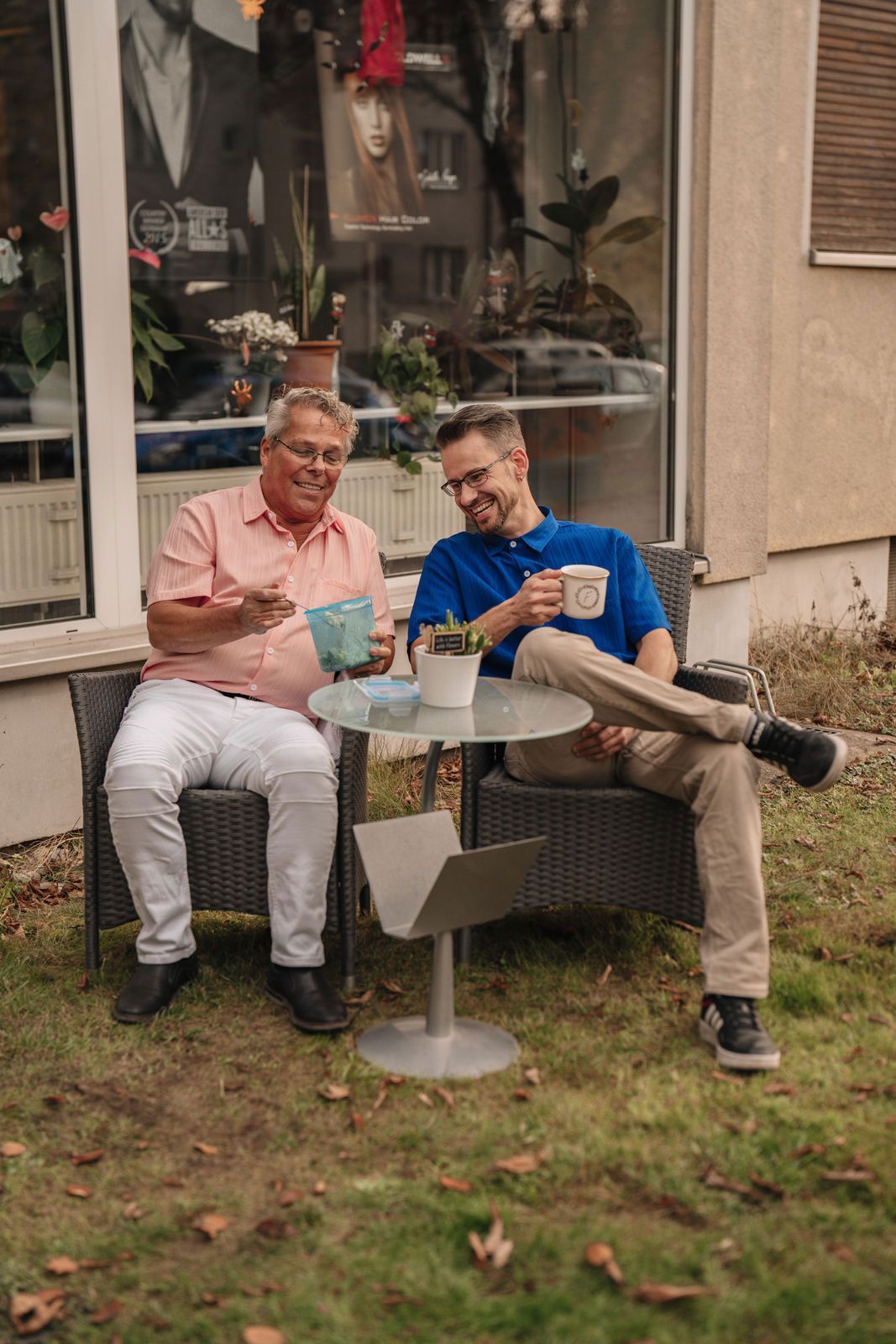 Zwei Männer sitzen an einem Tisch vor einem Gebäude.