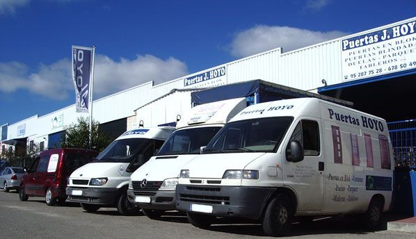 Una fila de camionetas blancas están estacionadas frente a un edificio que dice puertas rojas