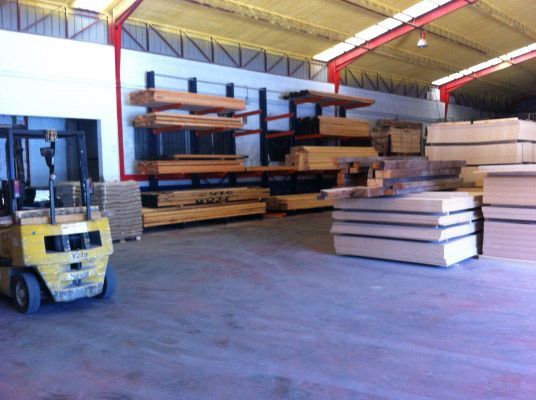 Un almacén lleno de mucha madera y una carretilla elevadora.