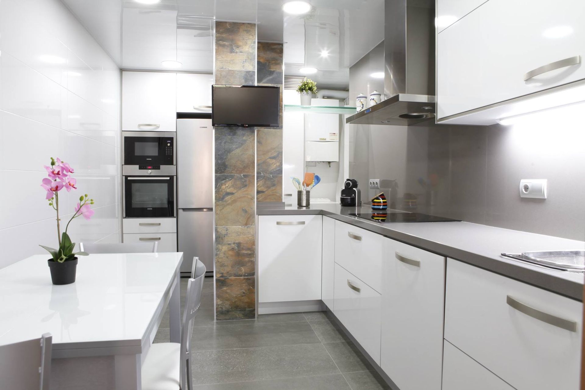 Cocina blanca moderna con electrodomésticos de acero inoxidable, encimeras grises y mesa de comedor.