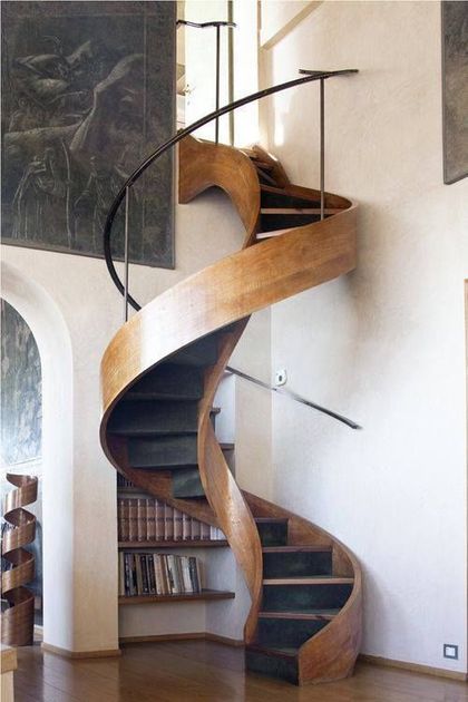 Escalera de caracol de madera en un interior luminoso, con pasamanos de metal negro y estanterías.