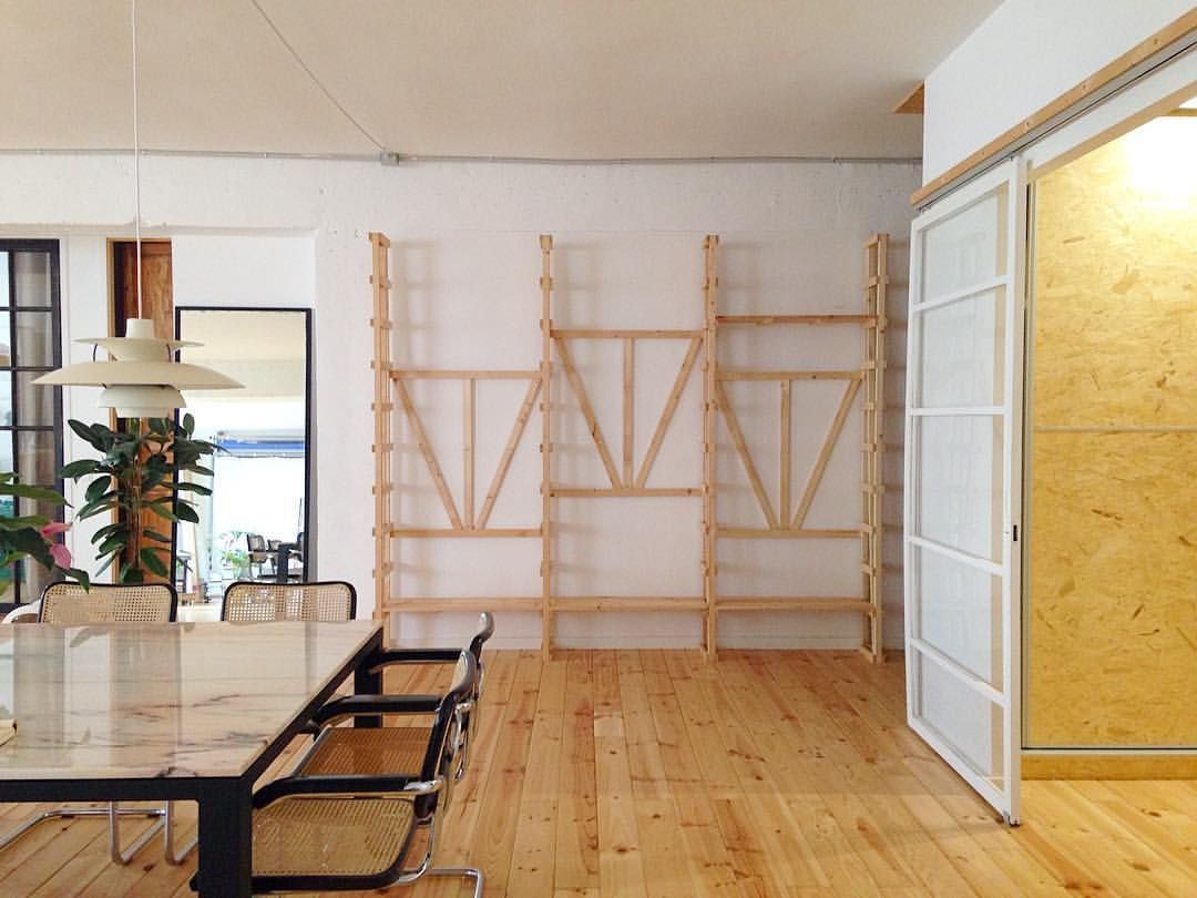 Habitación espaciosa con suelo de madera, mesa de comedor y estantería de madera sin terminar en la pared. Puerta abierta que da a una habitación más pequeña.