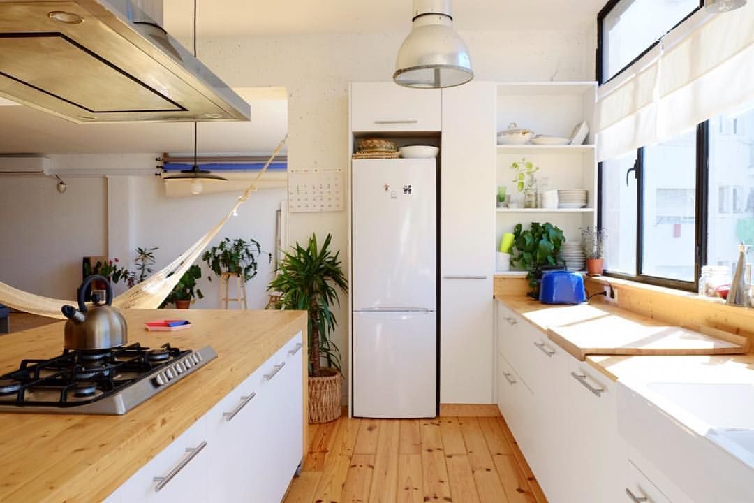 Cocina blanca brillante con encimeras de madera clara, electrodomésticos blancos y una ventana con luz natural.