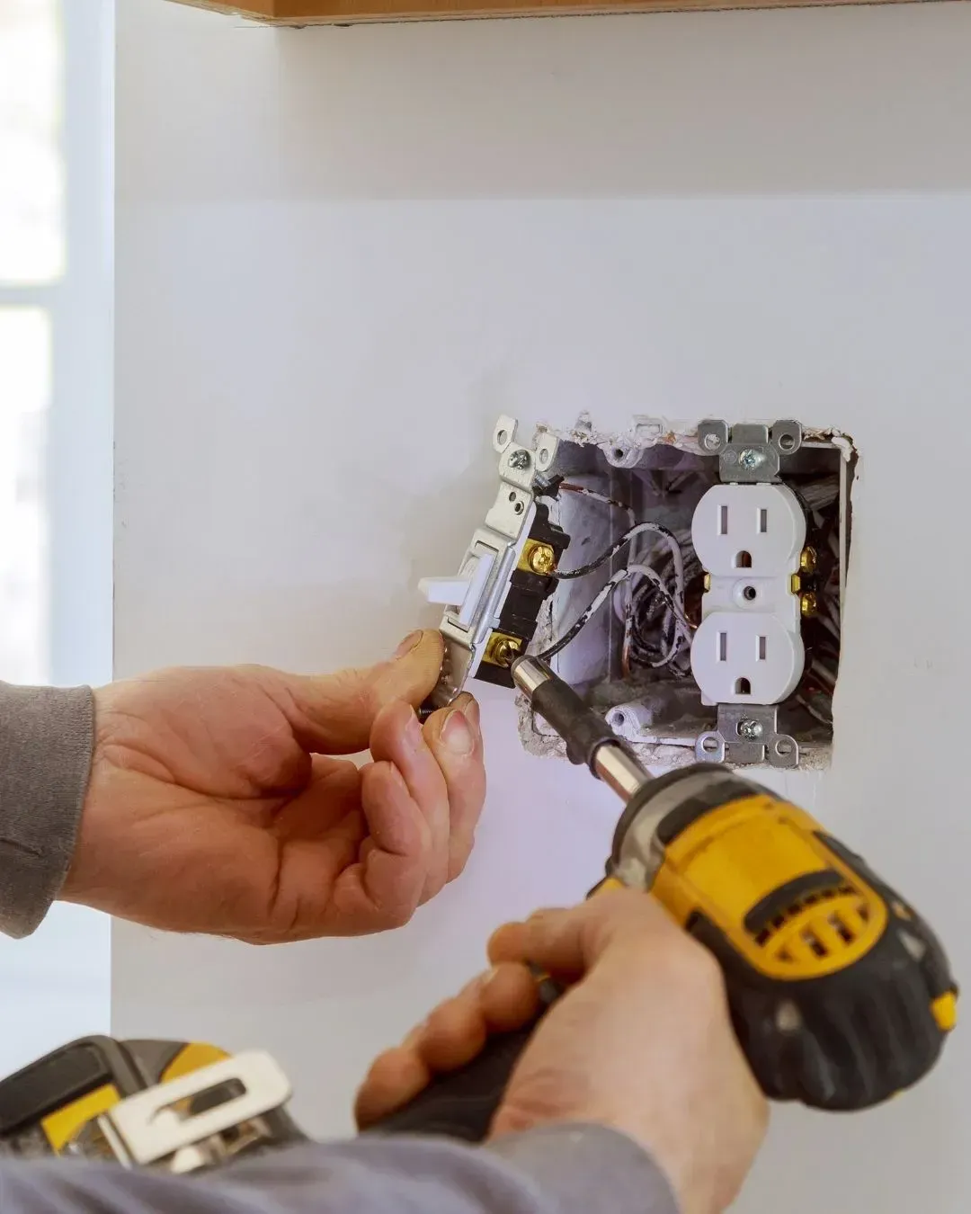 Persona instalando una toma de corriente eléctrica con un taladro en una pared blanca.