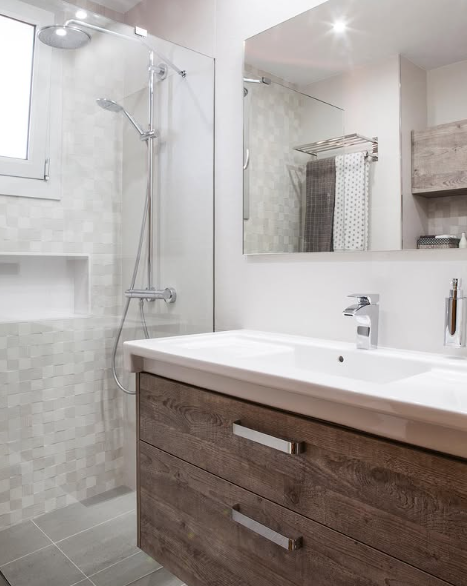 Baño moderno con tocador de madera, ducha y espejo grande.