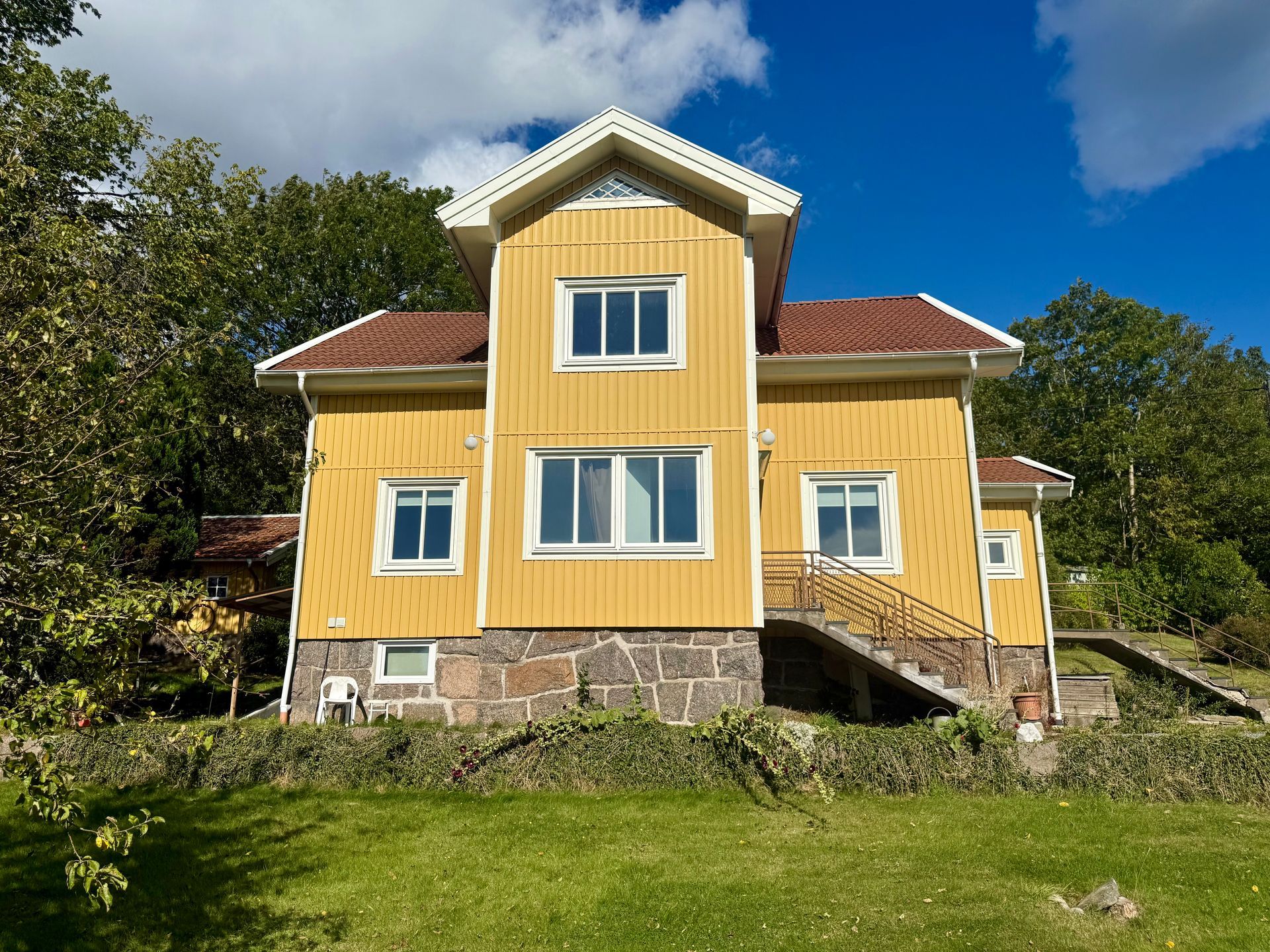 Yellow house with stone foundation, red roof, white trim, and a small staircase.