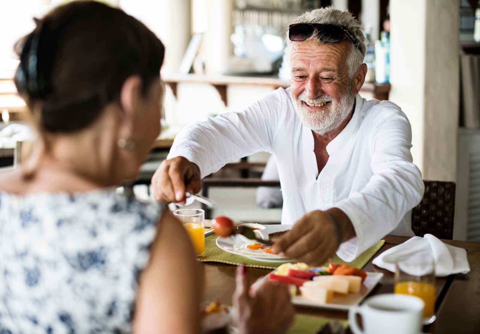 A smiling person serves food at a breakfast table with another person.