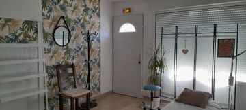 Pièce lumineuse avec papier peint à fleurs, des étagères blanches, une chaise, une porte d'entrée et une cloison vitrée.