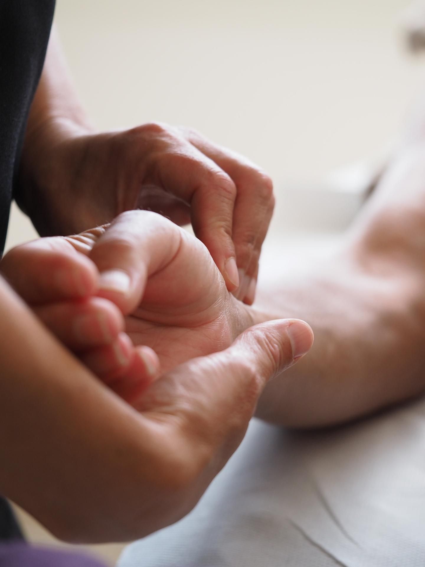 Des mains tenant délicatement un pied nu pendant un massage sur un lit moelleux.