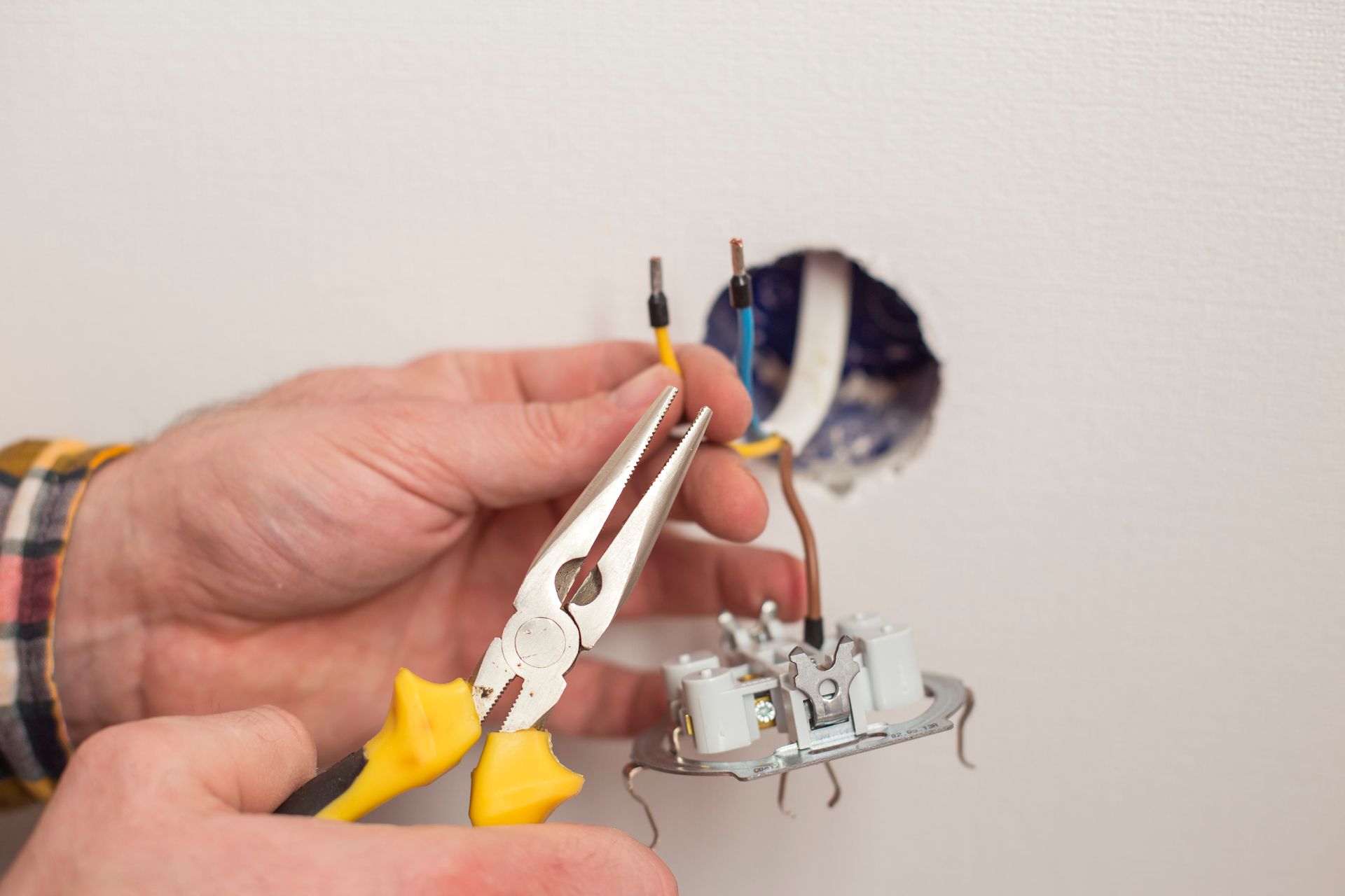 Des mains manipulent une pince pour travailler sur le câblage électrique d'un luminaire mural.