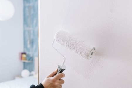 Une main utilise un rouleau à peinture pour appliquer de la peinture blanche sur un mur.