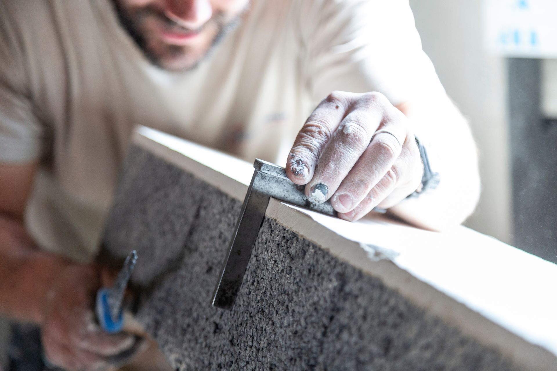 Une personne utilise une équerre pour mesurer le bord d'un morceau de matériau de construction gris et texturé.