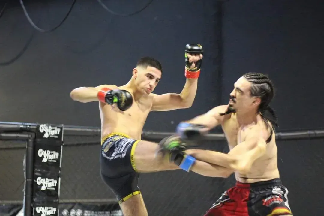 Dos kickboxers entrenando en un ring, uno de ellos vestido de azul conectando una patada a su oponente