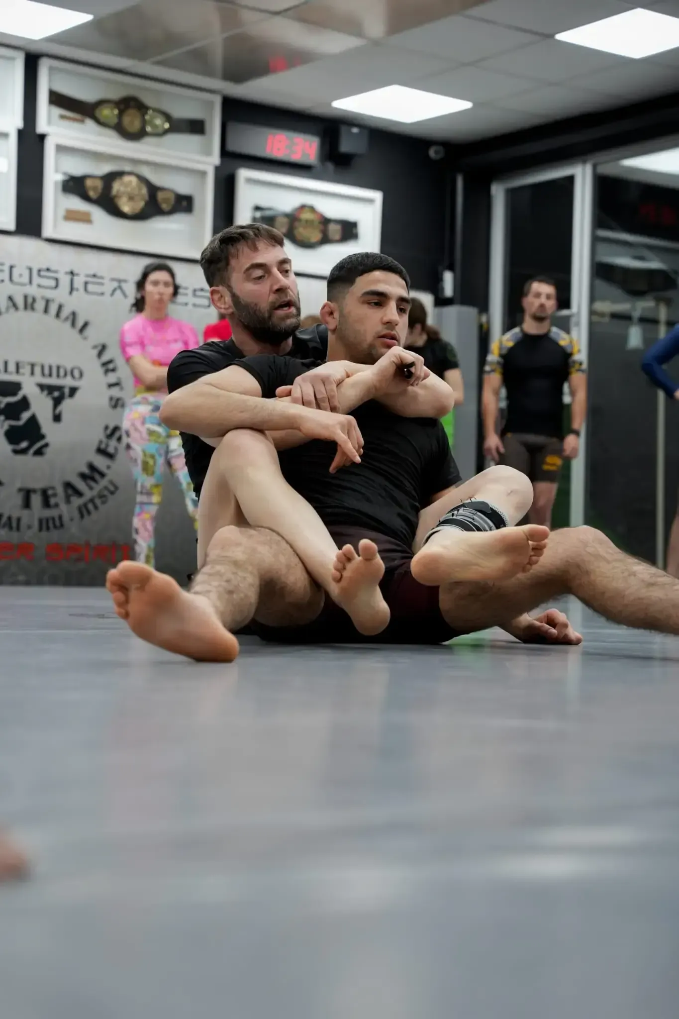 Dos luchadores forcejeando sobre una colchoneta amarilla bajo un telón de fondo rojo y azul.