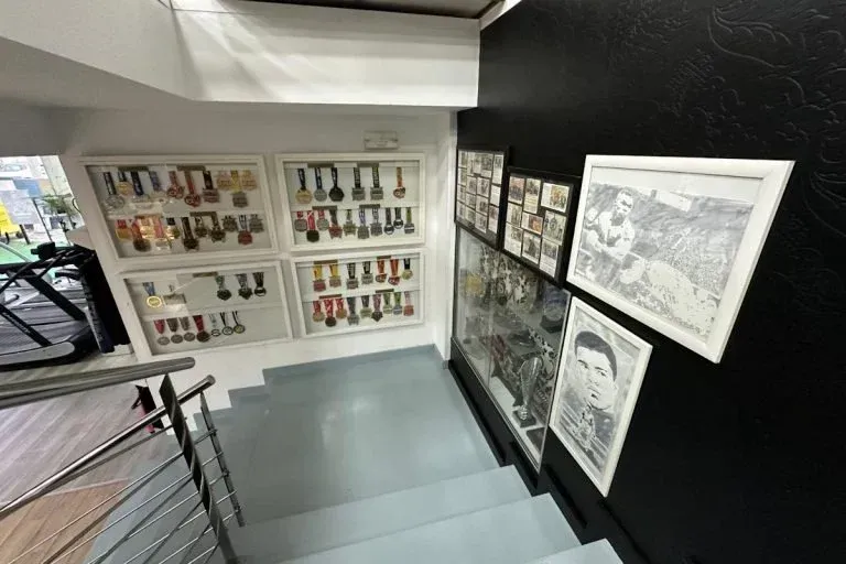 Escalera con dibujos en blanco y negro enmarcados y estantes con pequeños objetos en paredes blancas.