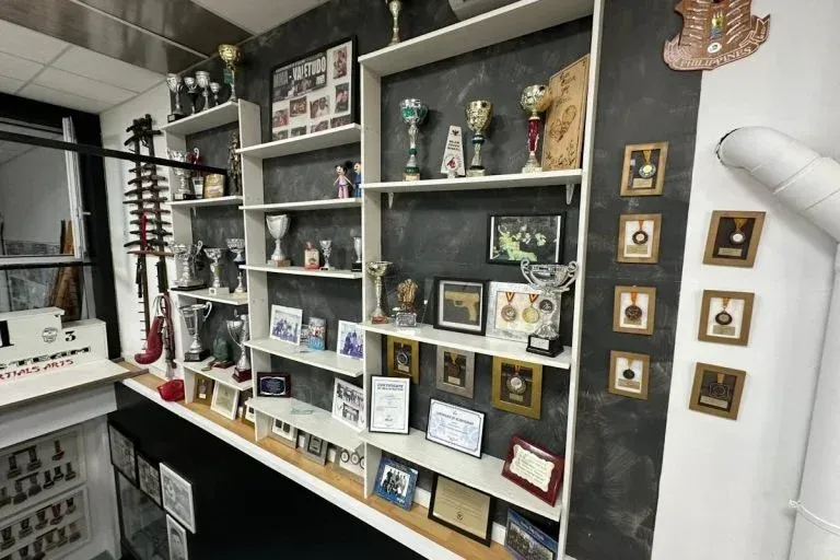 En una habitación se exhiben estantes con trofeos, placas y premios enmarcados.