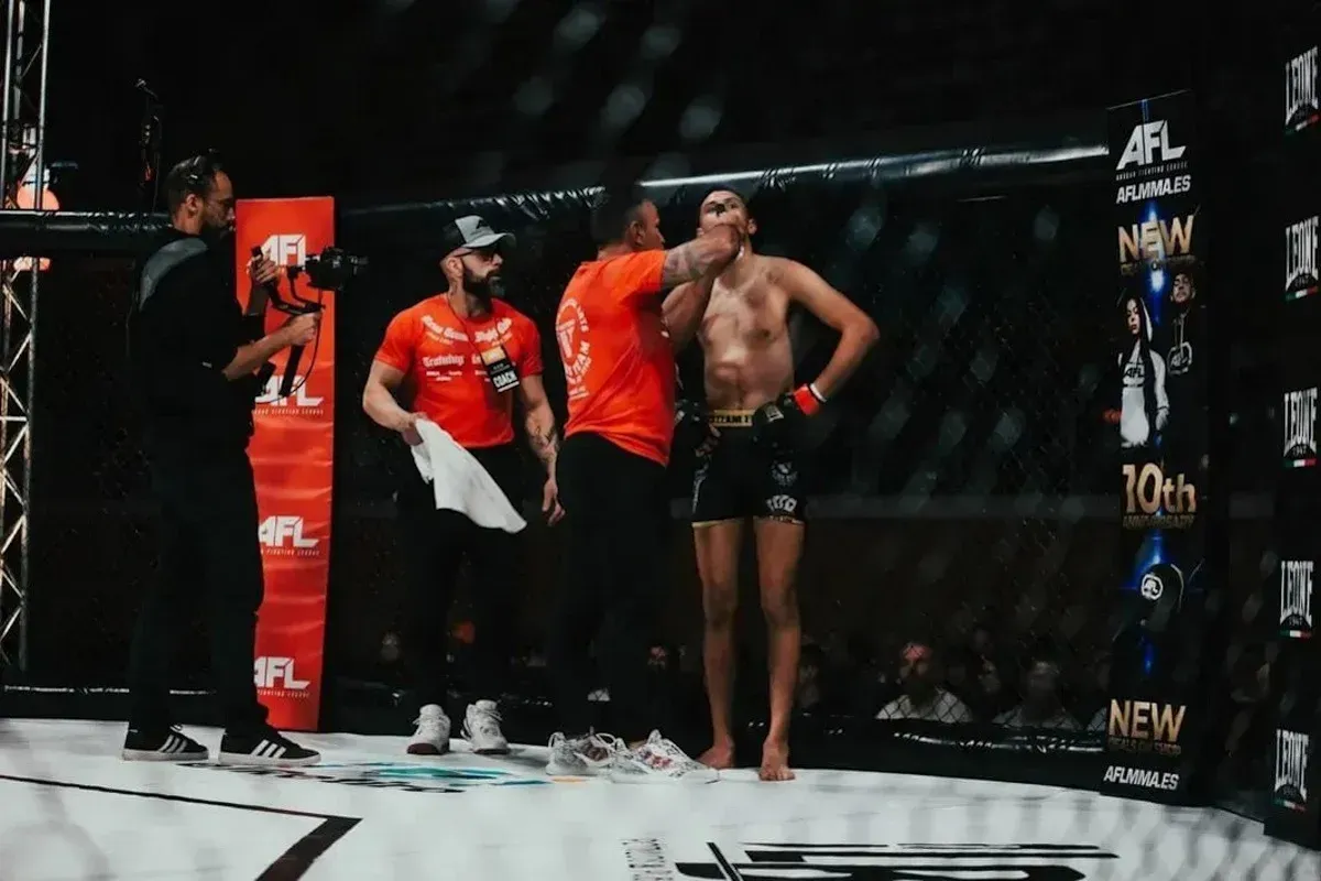 Un luchador de pie en el ring junto a un entrenador y un árbitro