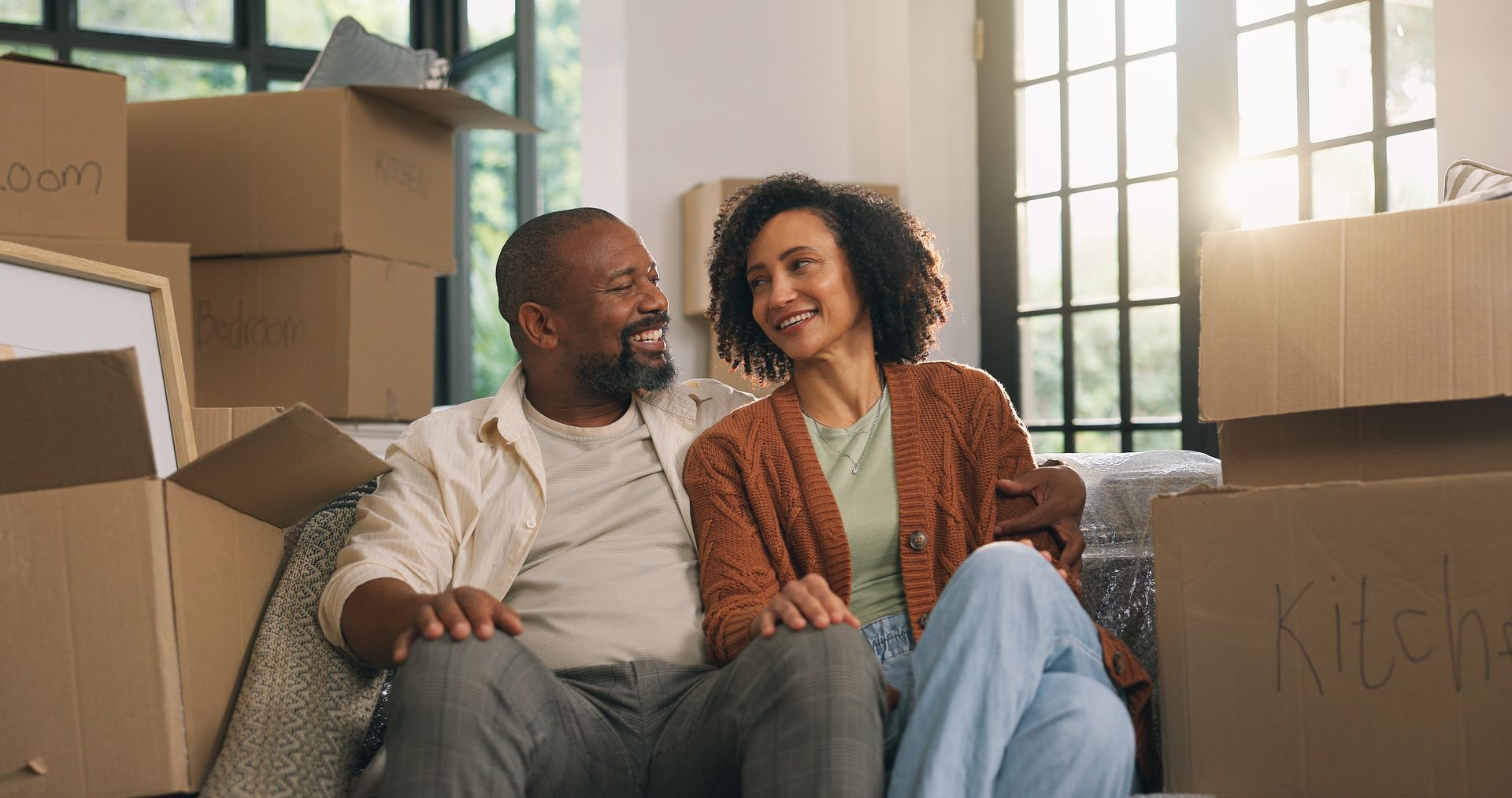 Un couple assis sur un canapé dans leur nouvelle maison, entouré de cartons de déménagement, souriant.