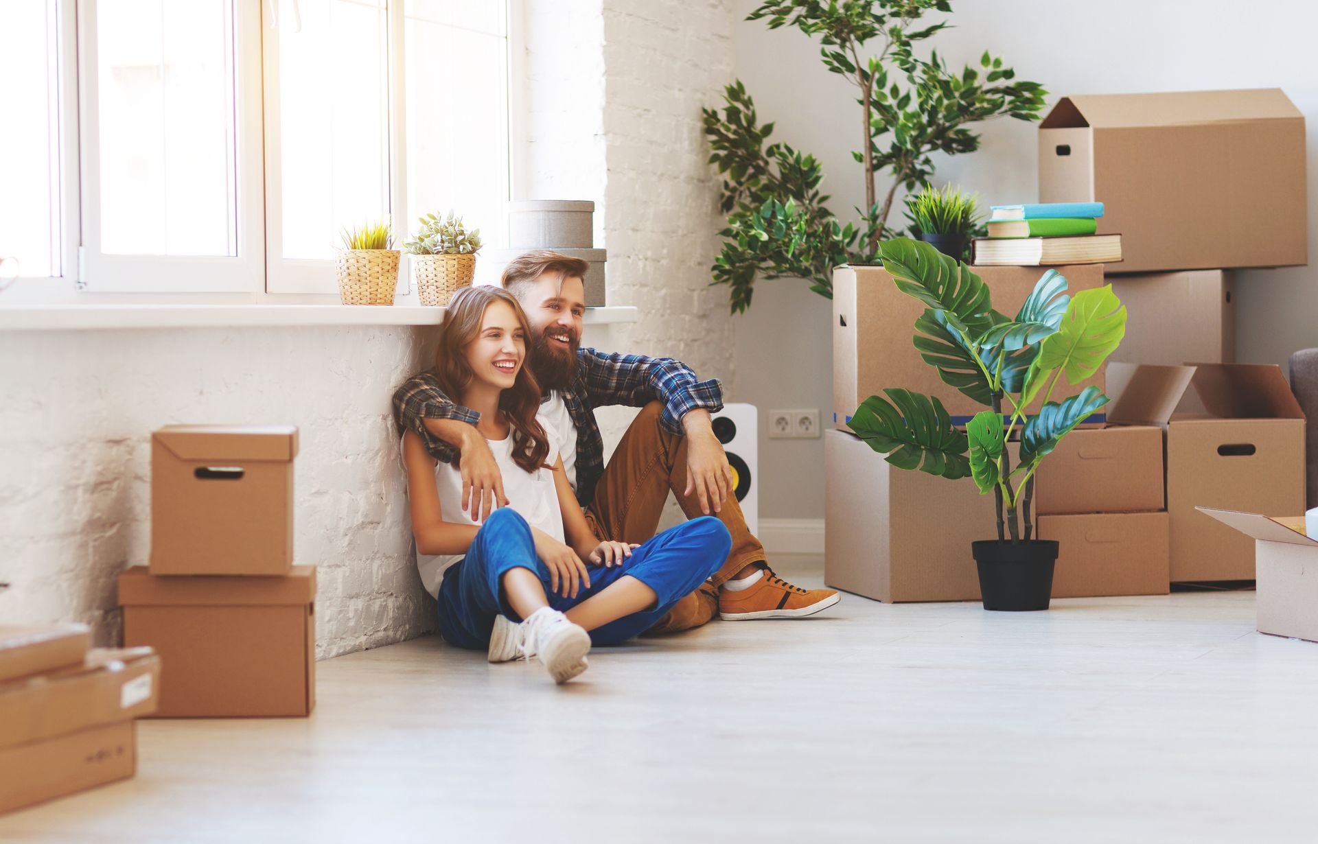 Un couple assis par terre dans leur nouvelle maison, entouré de cartons de déménagement, regardant par la fenêtre.
