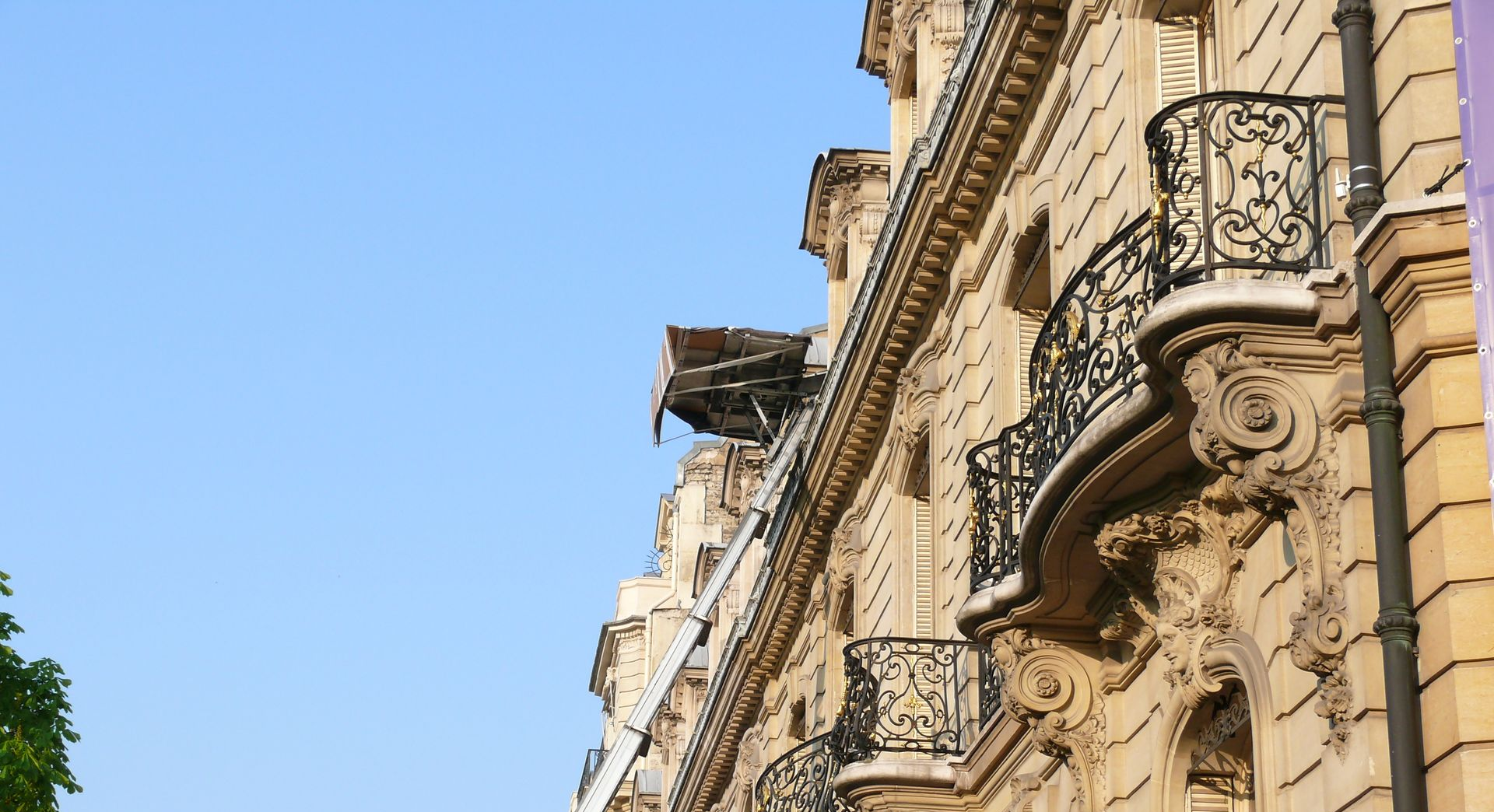 Façade d'immeuble ornée de balcons et de gargouilles se détachant sur un ciel bleu.
