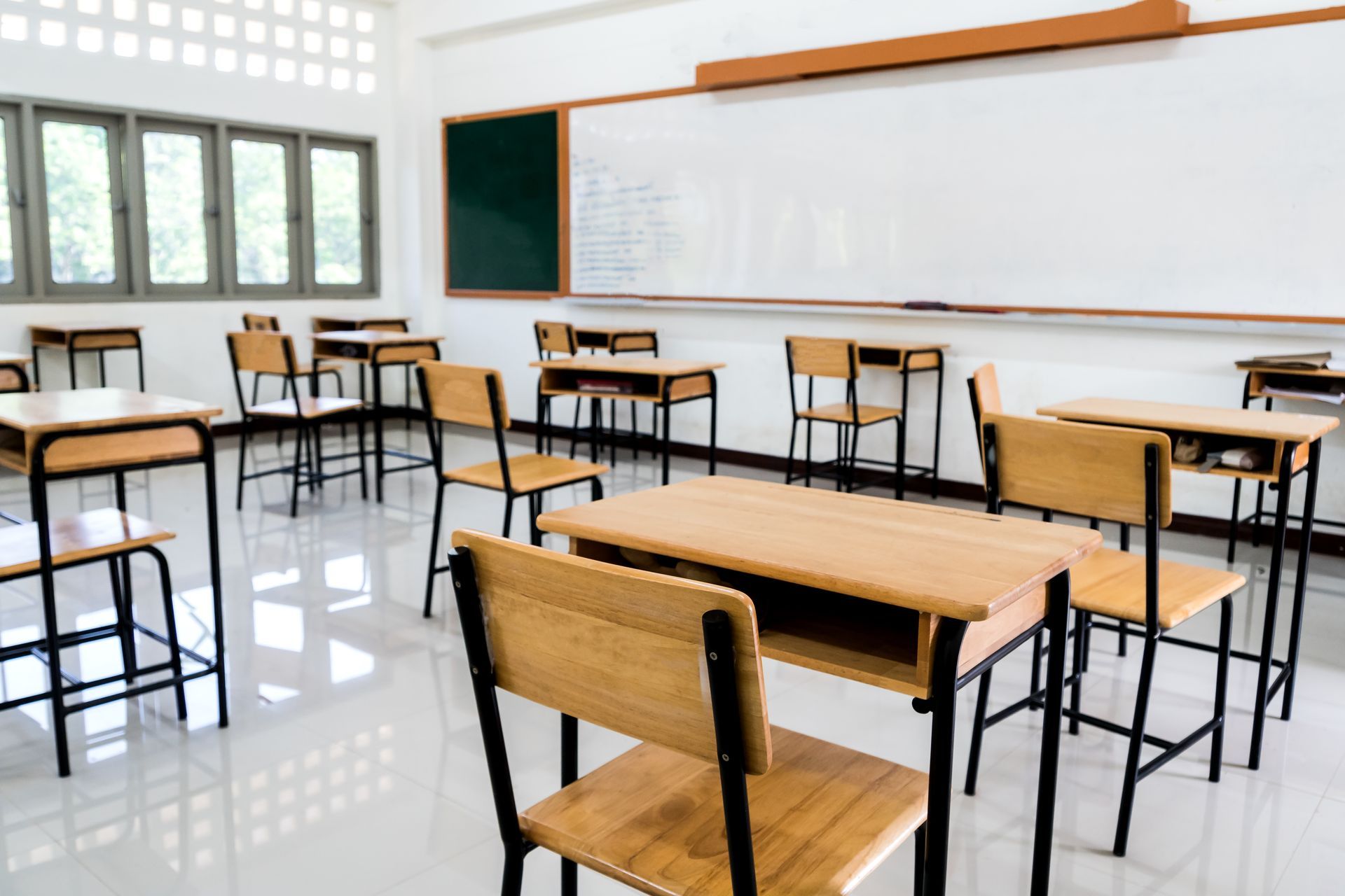 Salle de classe vide avec tables et chaises, tableaux blancs et fenêtres.