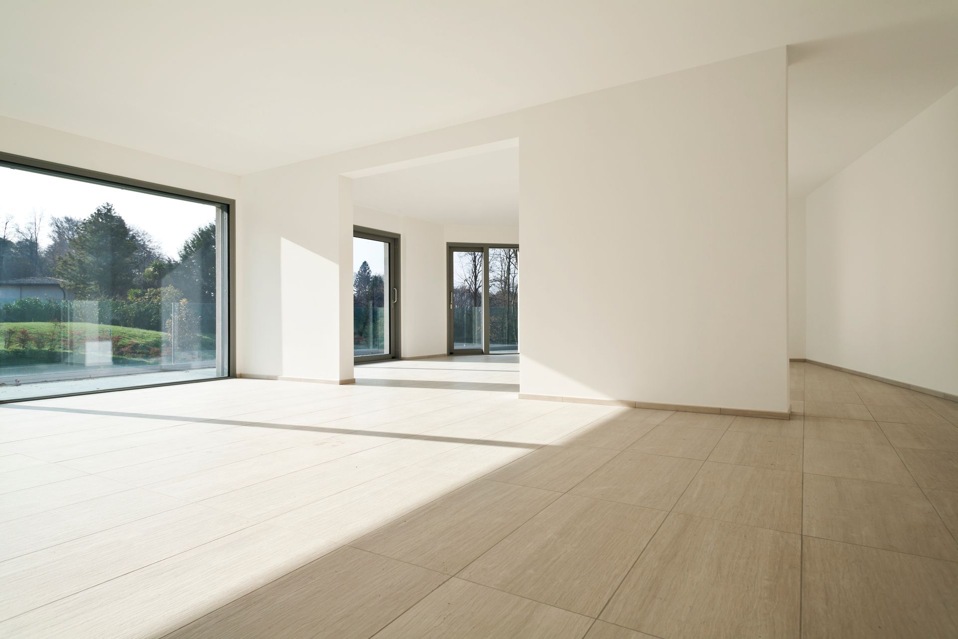Pièce vide avec de grandes fenêtres, des murs blancs et un parquet. Lumière naturelle abondante.