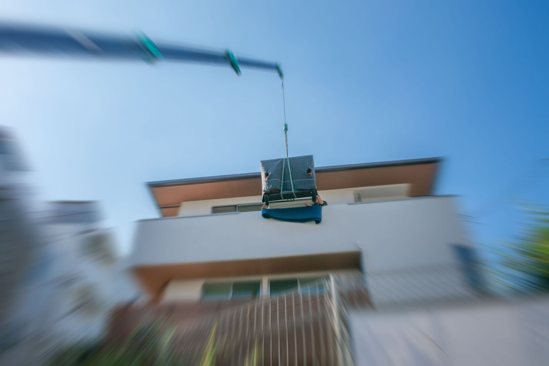 Une grue soulève un climatiseur sur le toit d'une maison, sur fond de ciel bleu.