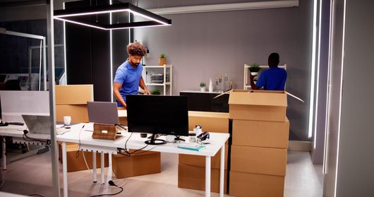 Deux personnes emballent des cartons dans un bureau, entourées de boîtes en carton.