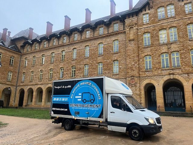 Un camion de déménagement est stationné devant un grand bâtiment ancien en pierre. Le camion arbore un logo bleu et blanc.