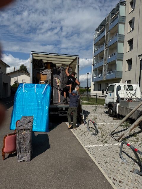 Des déménageurs chargent un camion de meubles devant un immeuble.
