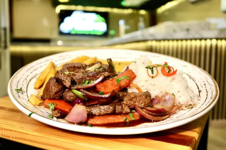 Plato de Lomo Saltado Peruano: carne de res salteada con cebolla, tomate, papas fritas y arroz.