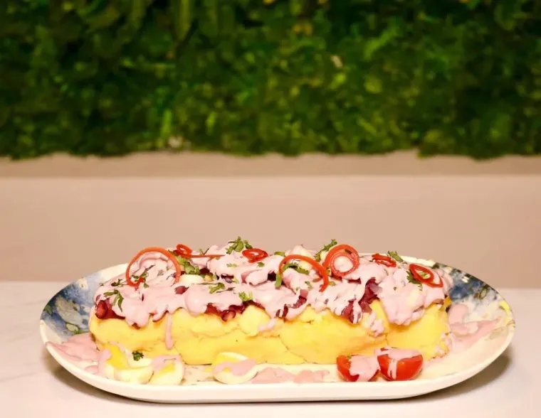 Plato de pan de maíz relleno, cubierto con salsa rosa y pimientos rojos en rodajas, sobre un fondo verde.