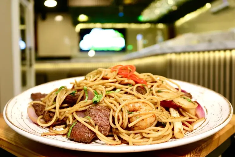 Plato de espaguetis con carne, camarones y verduras en un entorno de restaurante.