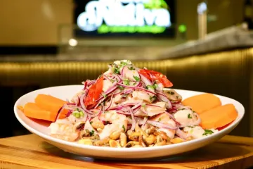 Ceviche en plato blanco con cebolla morada, cilantro y rodajas de camote.